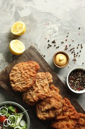 Tasty schnitzels served with lemon, salad and sauce on grey table, flat lay