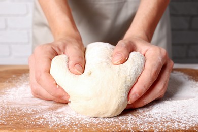 Woman kneading dough at wooden table, closeup