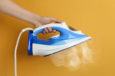 Woman holding modern iron with steam on orange background, closeup