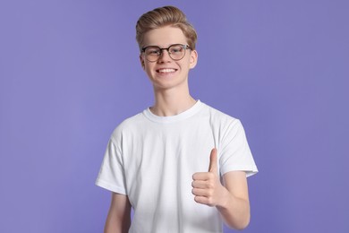 Photo of Teenage boy showing thumb up on purple background