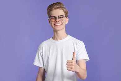 Teenage boy showing thumb up on purple background