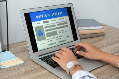 Woman using laptop to fill driver's license application form at table in office, closeup