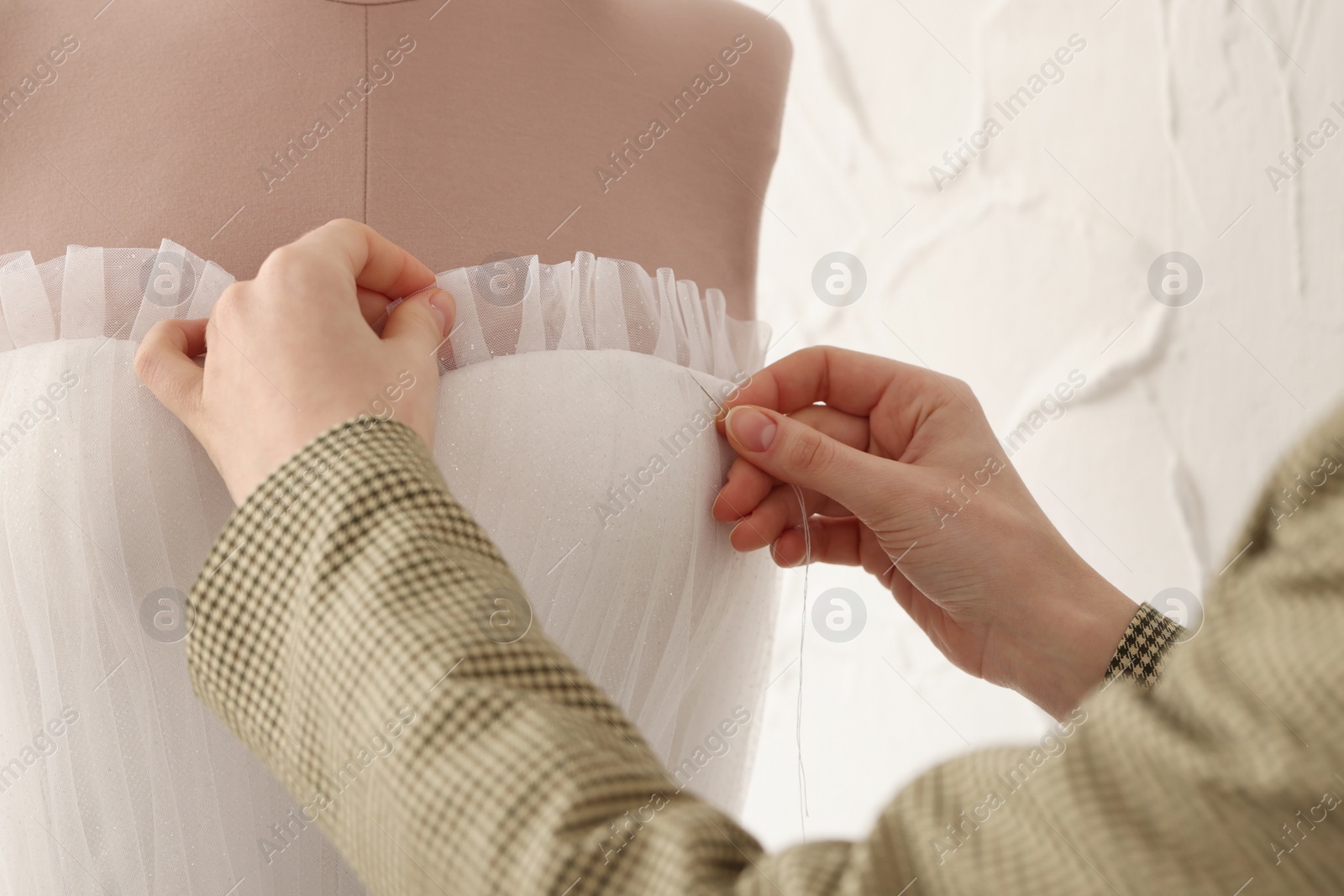 Photo of Dressmaker working with wedding dress on mannequin in atelier, closeup