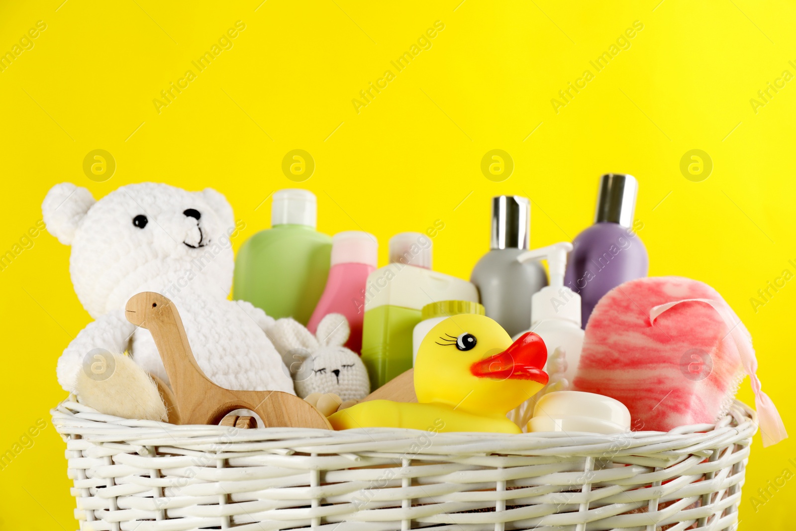 Photo of Wicker basket with baby cosmetic products and accessories on yellow background