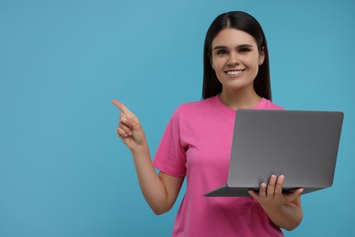 Special promotion. Happy woman with laptop pointing at something on light blue background, space for text