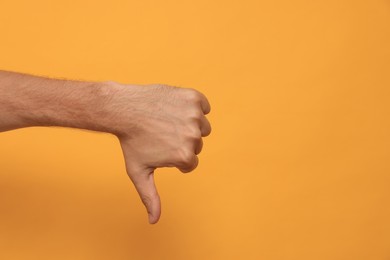 Photo of Man showing thumb down on orange background, closeup. Space for text