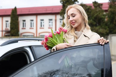 Happy young woman with beautiful bouquet near car outdoors