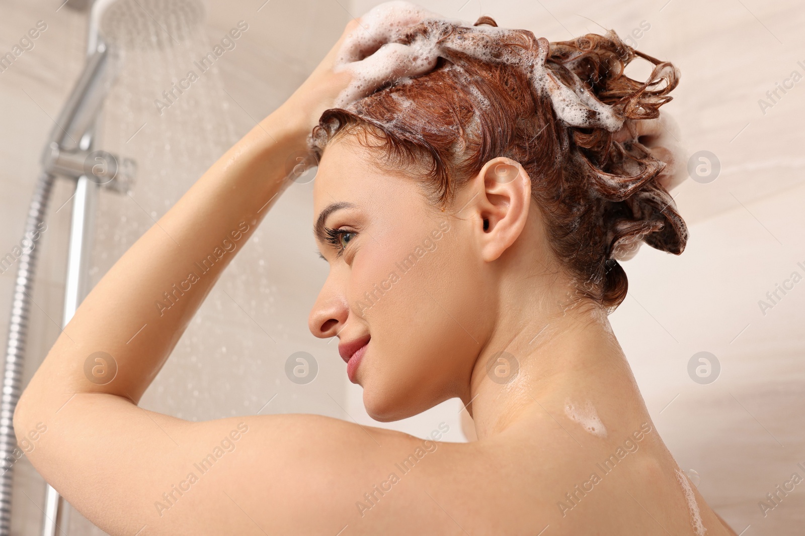 Photo of Young woman washing her hair with shampoo in shower