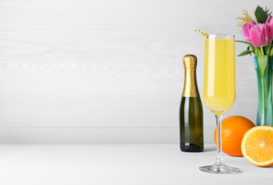 Photo of Glass of Mimosa cocktail on white table. Space for text