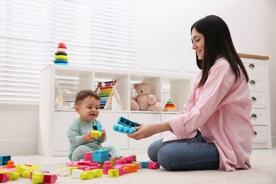 Cute baby boy playing with mother and building blocks on floor at home