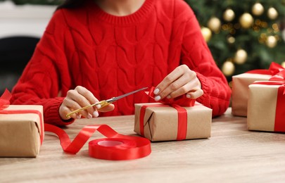 Photo of Woman decorating Christmas gift box at wooden table indoors, closeup