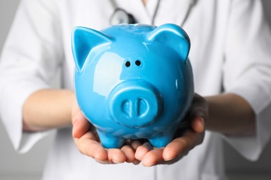 Photo of Doctor holding light blue ceramic piggy bank, closeup. Medical insurance