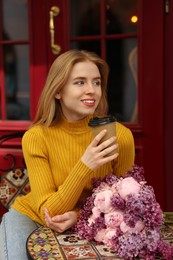 Beautiful woman with bouquet of spring flowers and coffee in outdoor cafe