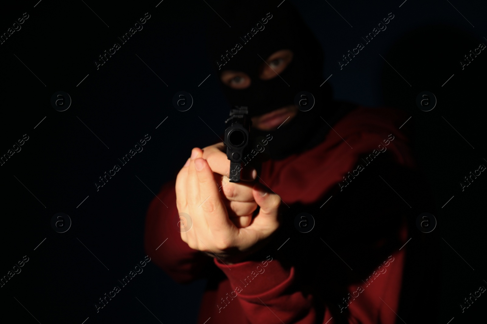 Photo of Man in mask holding gun on dark background, focus on hands