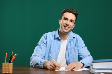 Portrait of male teacher working at table against color background