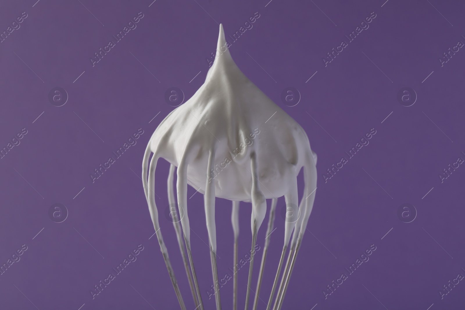 Photo of Whisk with whipped cream on violet background, closeup