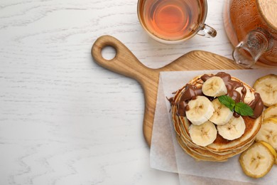 Photo of Tasty pancakes with sliced banana served on white wooden table, flat lay. Space for text
