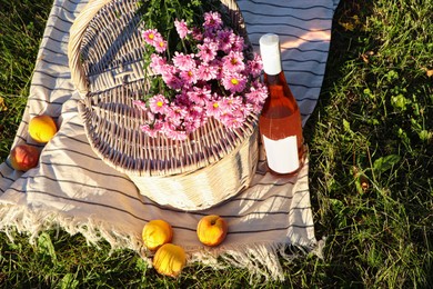 Photo of Picnic basket, flowers, peaches and bottle of wine on blanket outdoors