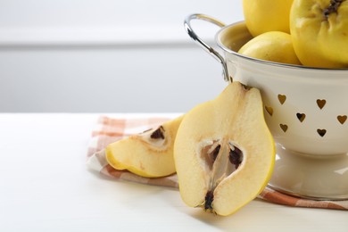 Photo of Tasty ripe quinces and metal colander on white wooden table, closeup. Space for text