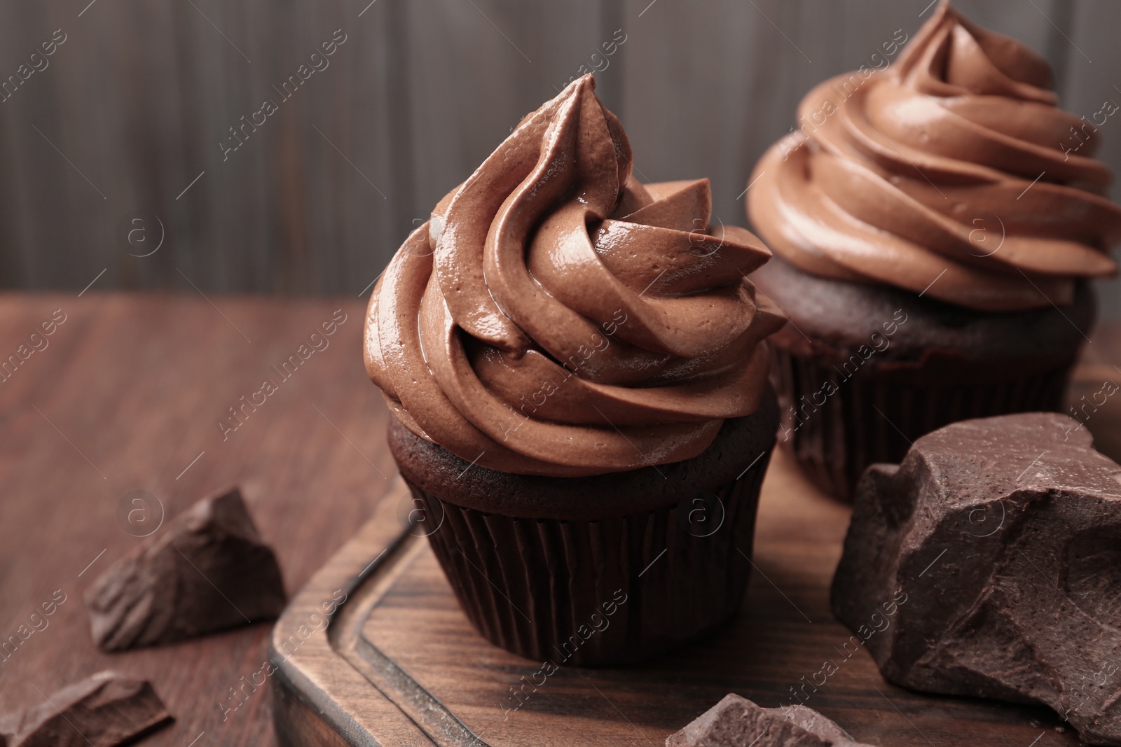 Photo of Delicious cupcakes with cream and chocolate pieces on wooden table, closeup