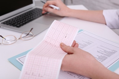 Photo of Doctor examining cardiogram at table in clinic, closeup