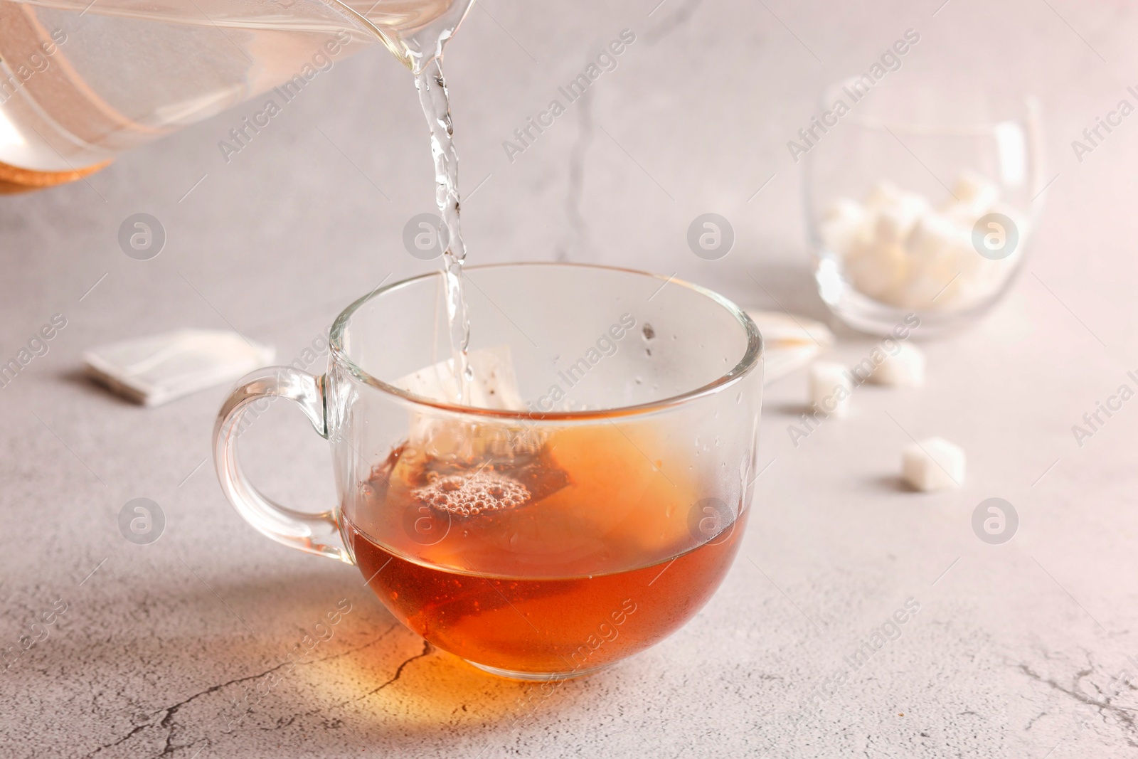 Photo of Pouring hot water into cup with tea bag on light grey textured table, closeup