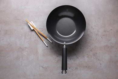 Empty iron wok and chopsticks on grey table, flat lay