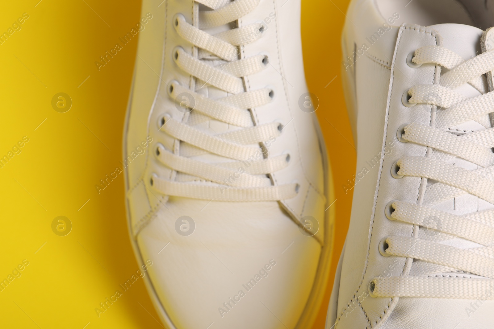 Photo of Pair of stylish white sneakers on yellow background, closeup