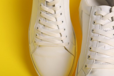 Photo of Pair of stylish white sneakers on yellow background, closeup