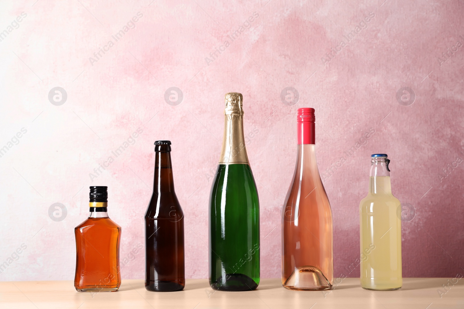Photo of Bottles with different alcoholic drinks on table against color background