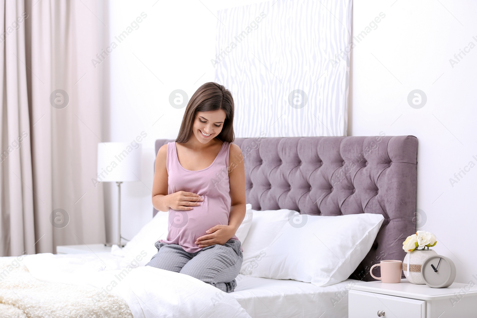 Photo of Happy pregnant woman sitting on bed at home