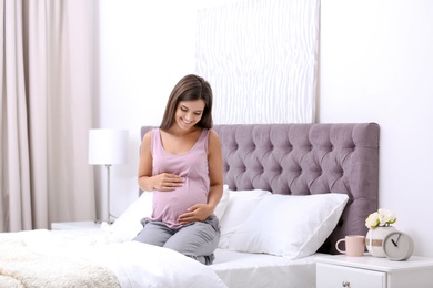 Happy pregnant woman sitting on bed at home