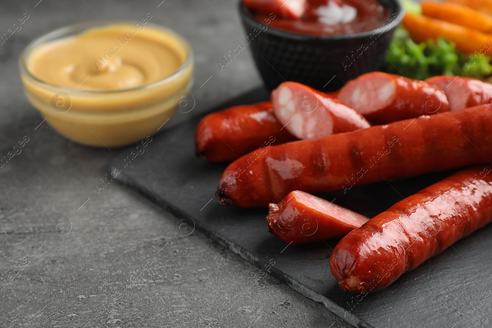 Photo of Delicious grilled sausages and vegetables on grey table, closeup. Space for text