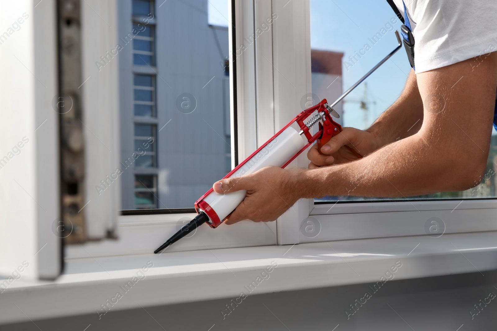 Photo of Worker sealing plastic window with caulk indoors, closeup. Installation process