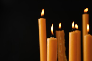 Photo of Many burning church candles on black background, space for text