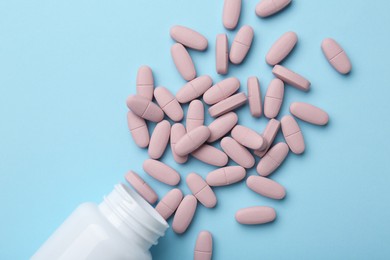 Vitamin pills and bottle on light blue background, top view