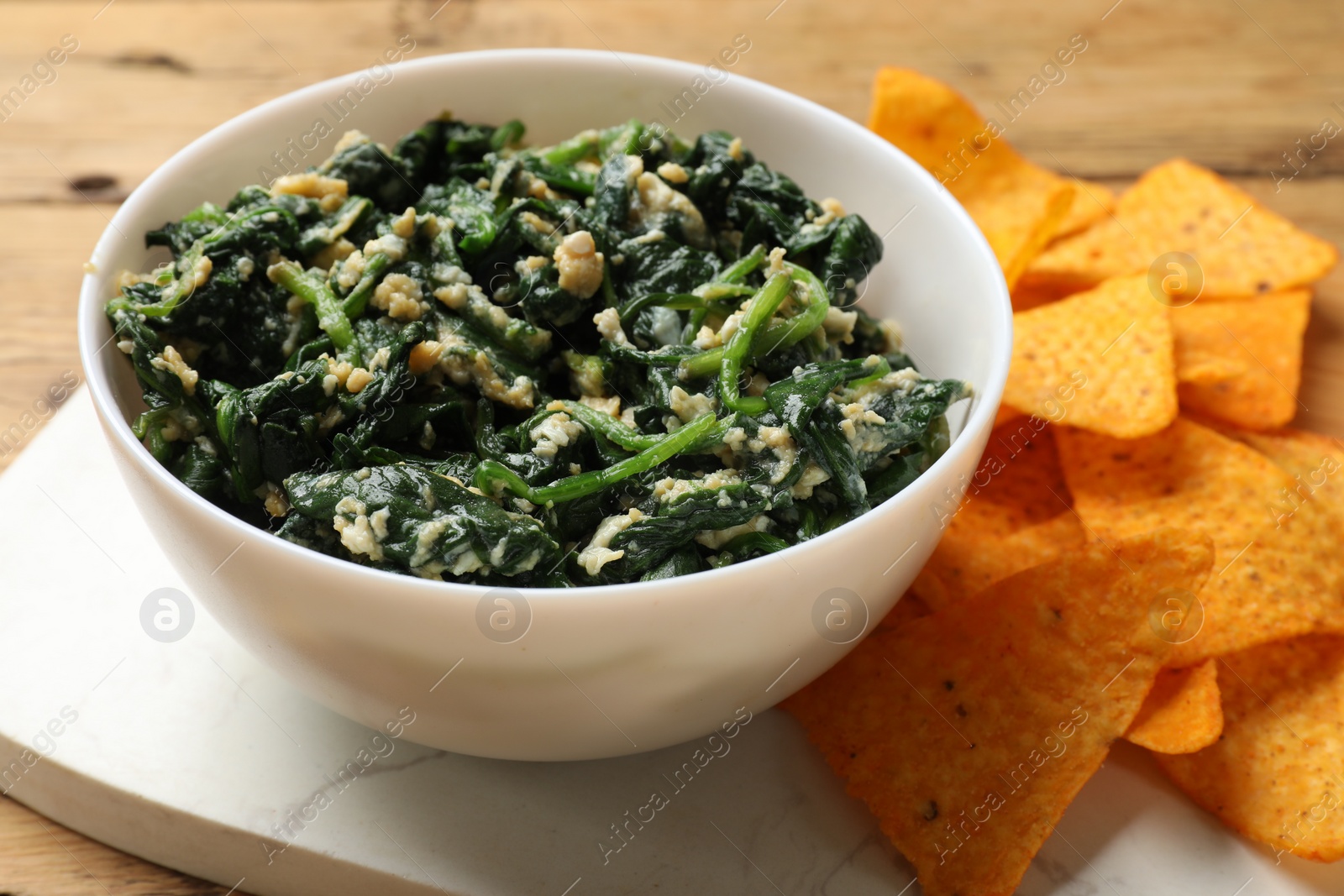 Photo of Tasty spinach dip with eggs in bowl and nachos chips on wooden table, closeup