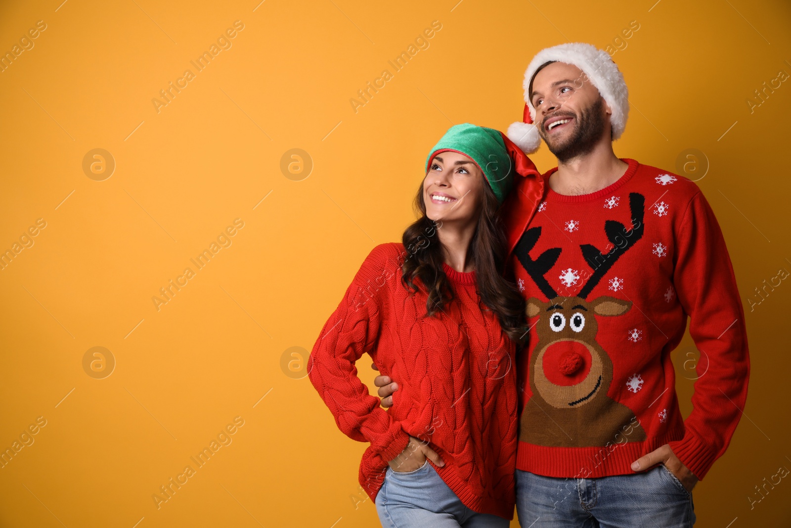 Photo of Young couple in Christmas sweaters and hats on yellow background. Space for text