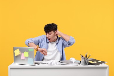 Emotional young man working at white table on orange background. Deadline concept