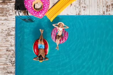 Image of Happy couple with inflatable rings in swimming pool, top view. Summer vacation