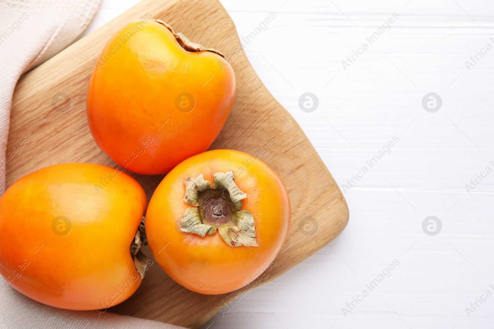 Photo of Board with delicious ripe persimmons on white wooden table, top view. Space for text