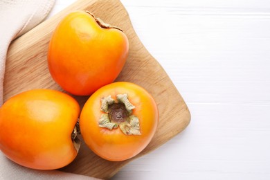 Photo of Board with delicious ripe persimmons on white wooden table, top view. Space for text