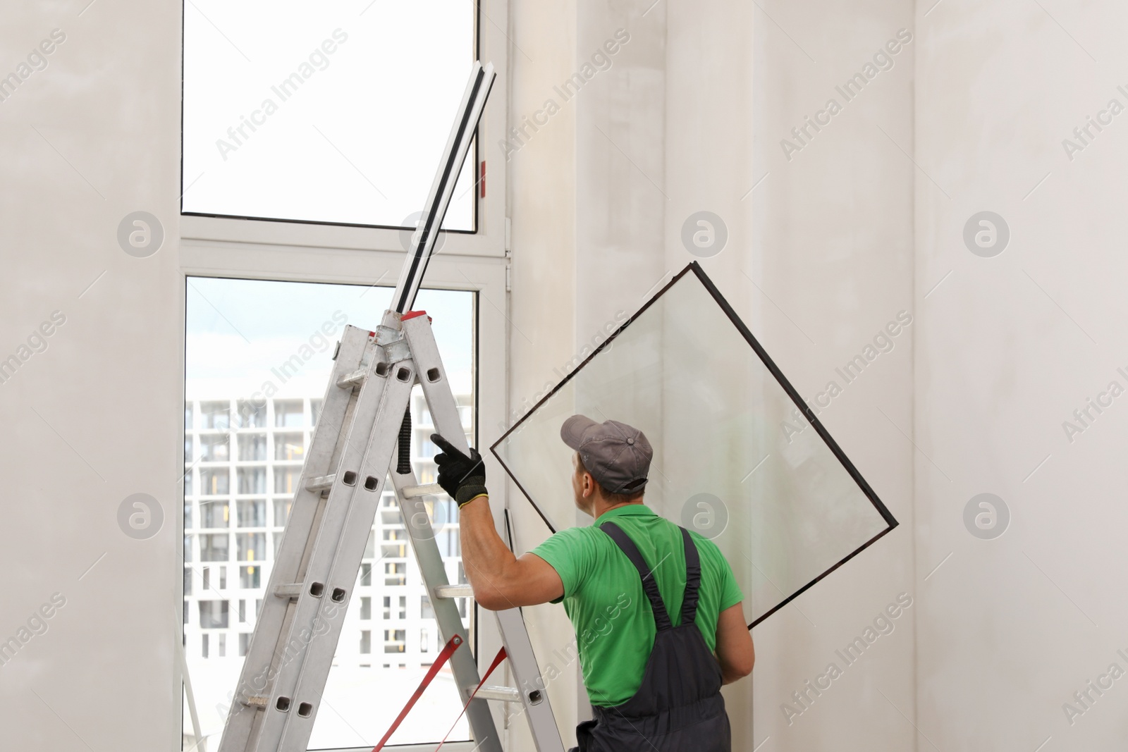 Photo of Worker in uniform holding double glazing window indoors, back view