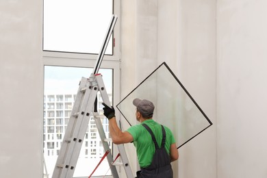 Worker in uniform holding double glazing window indoors, back view