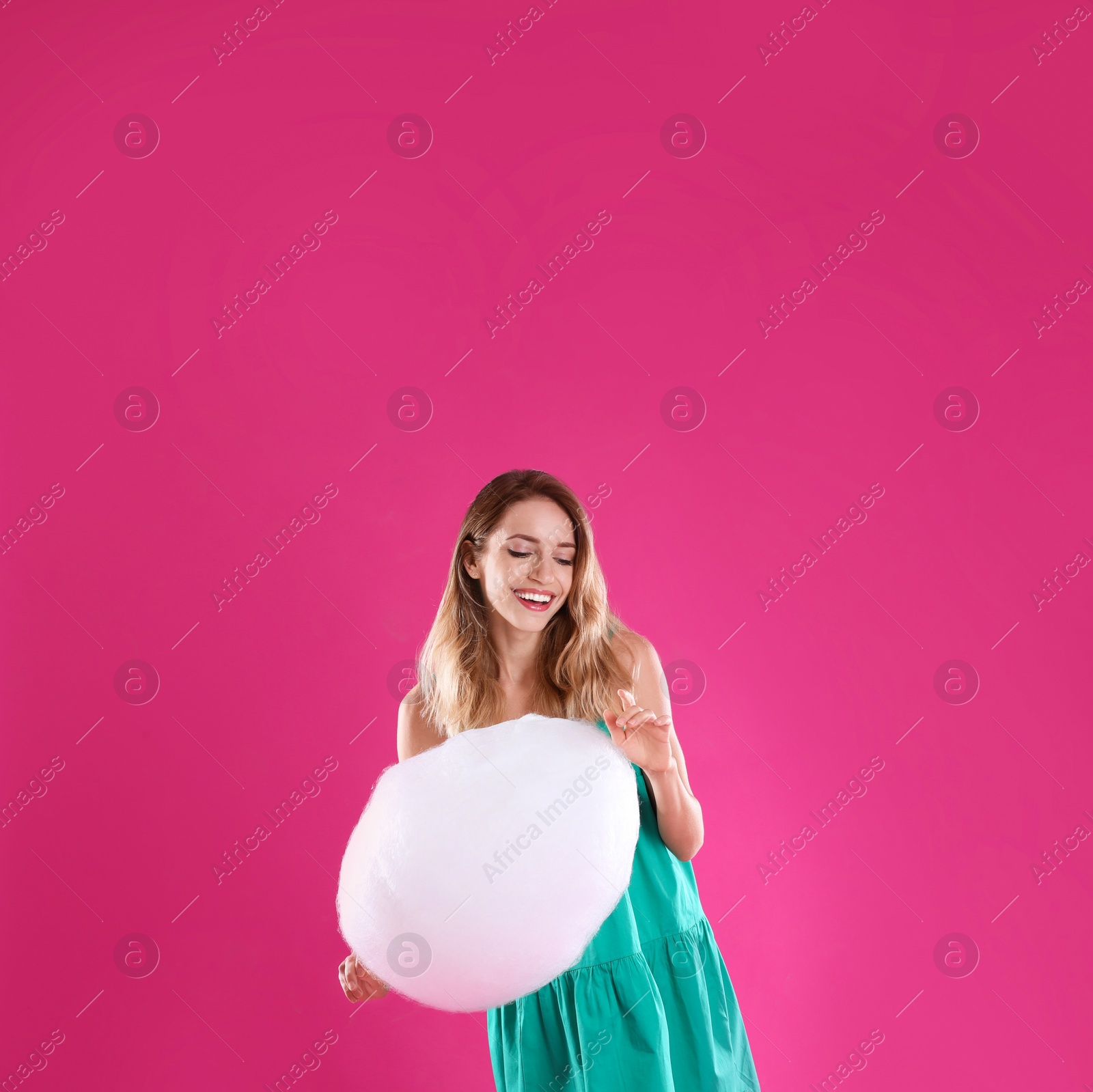 Photo of Happy young woman with cotton candy on pink background