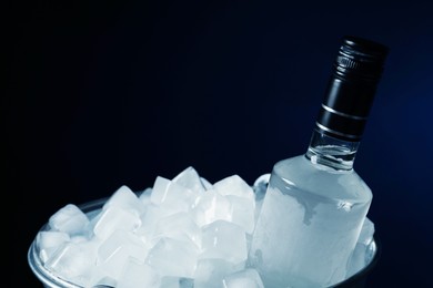 Photo of Bottle of vodka in metal bucket with ice on black background, closeup. Space for text