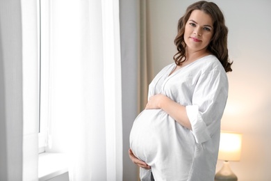 Young pregnant woman near window at home