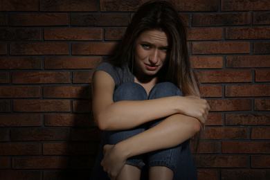 Abused young woman crying near brick wall. Domestic violence concept