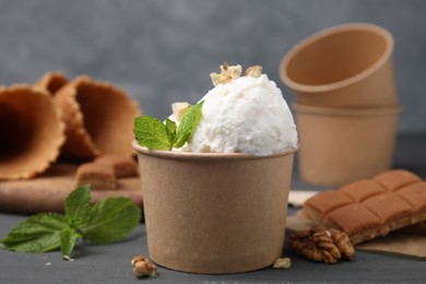 Tasty ice cream with mint and nuts in paper cup on grey table, closeup