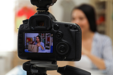 Fashion blogger recording new video at table indoors, focus on camera